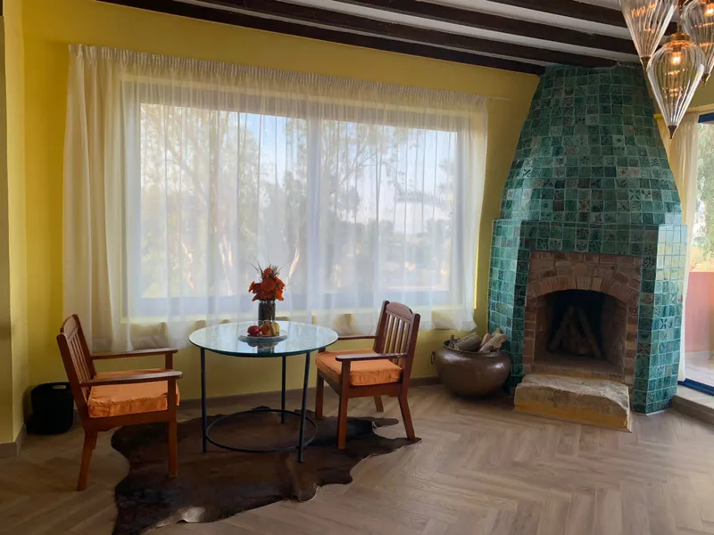 Living room with a green-tiled fireplace and a table by the window