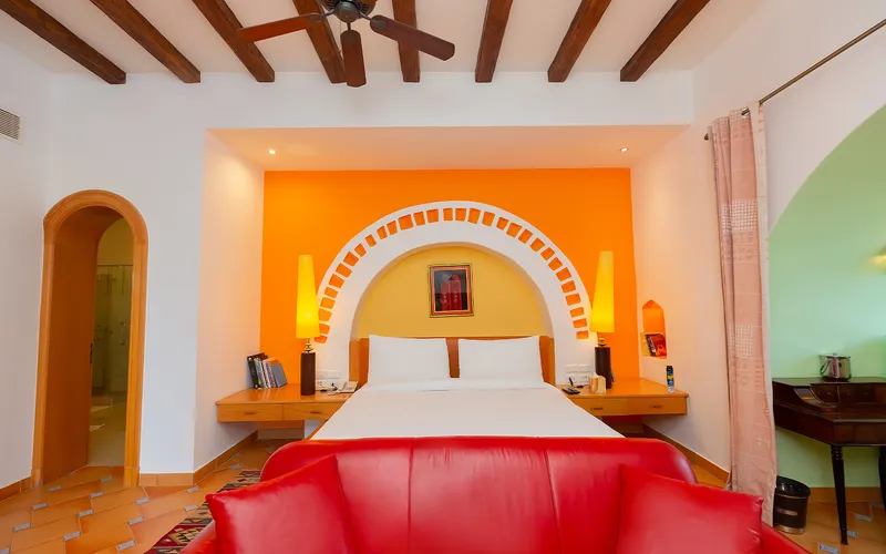 Bed under a white brick arch on an orange wall, with a red sofa in front