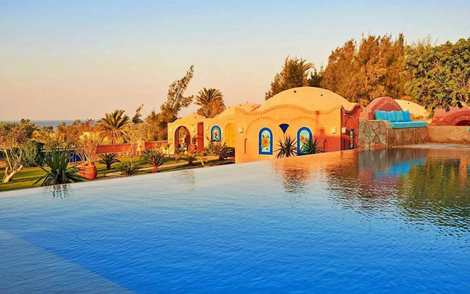 Terracotta domed rooms reflected in an infinity pool at golden hour.