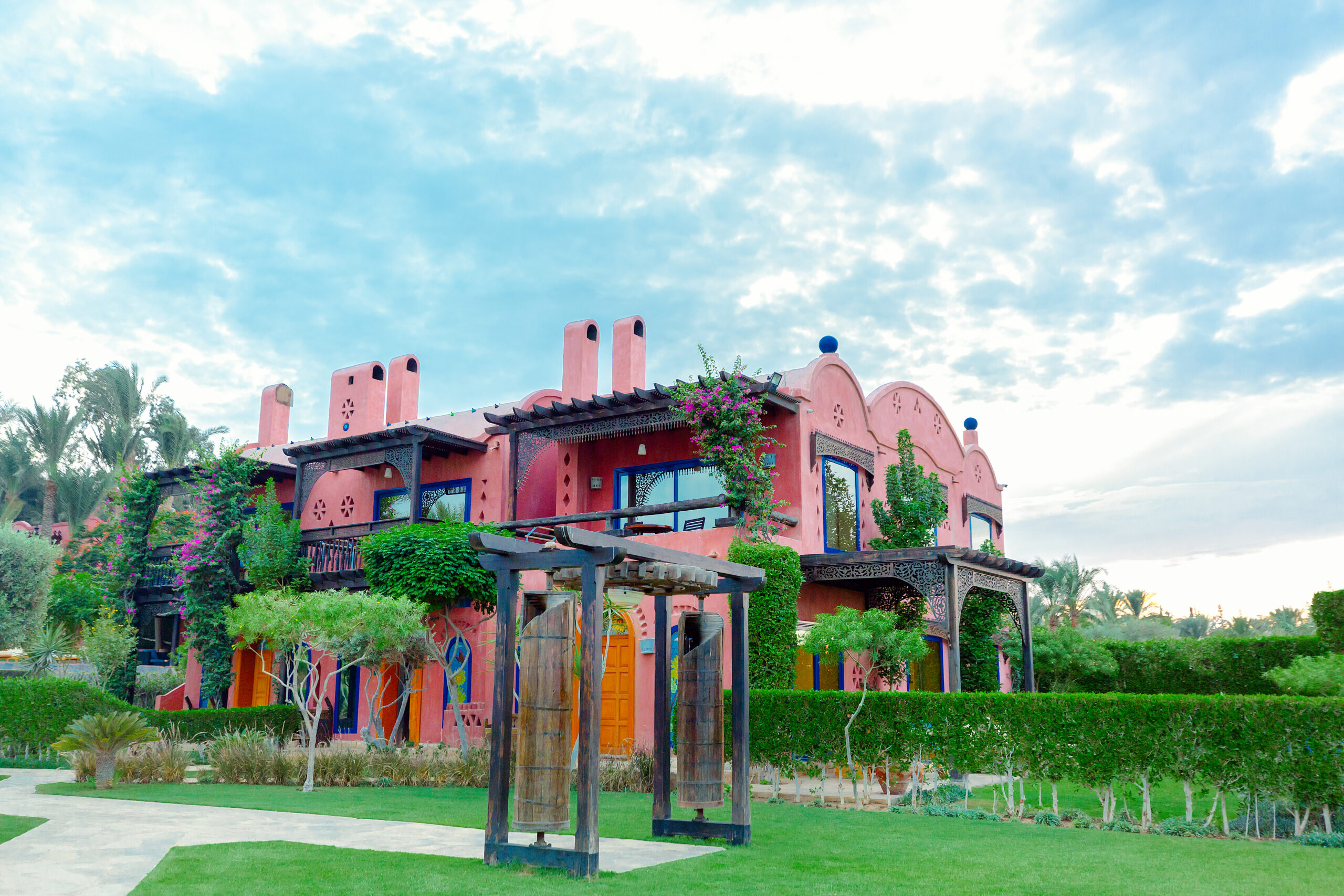 Two-storey pink villa with carved wooden balconies and bougainvillea.
